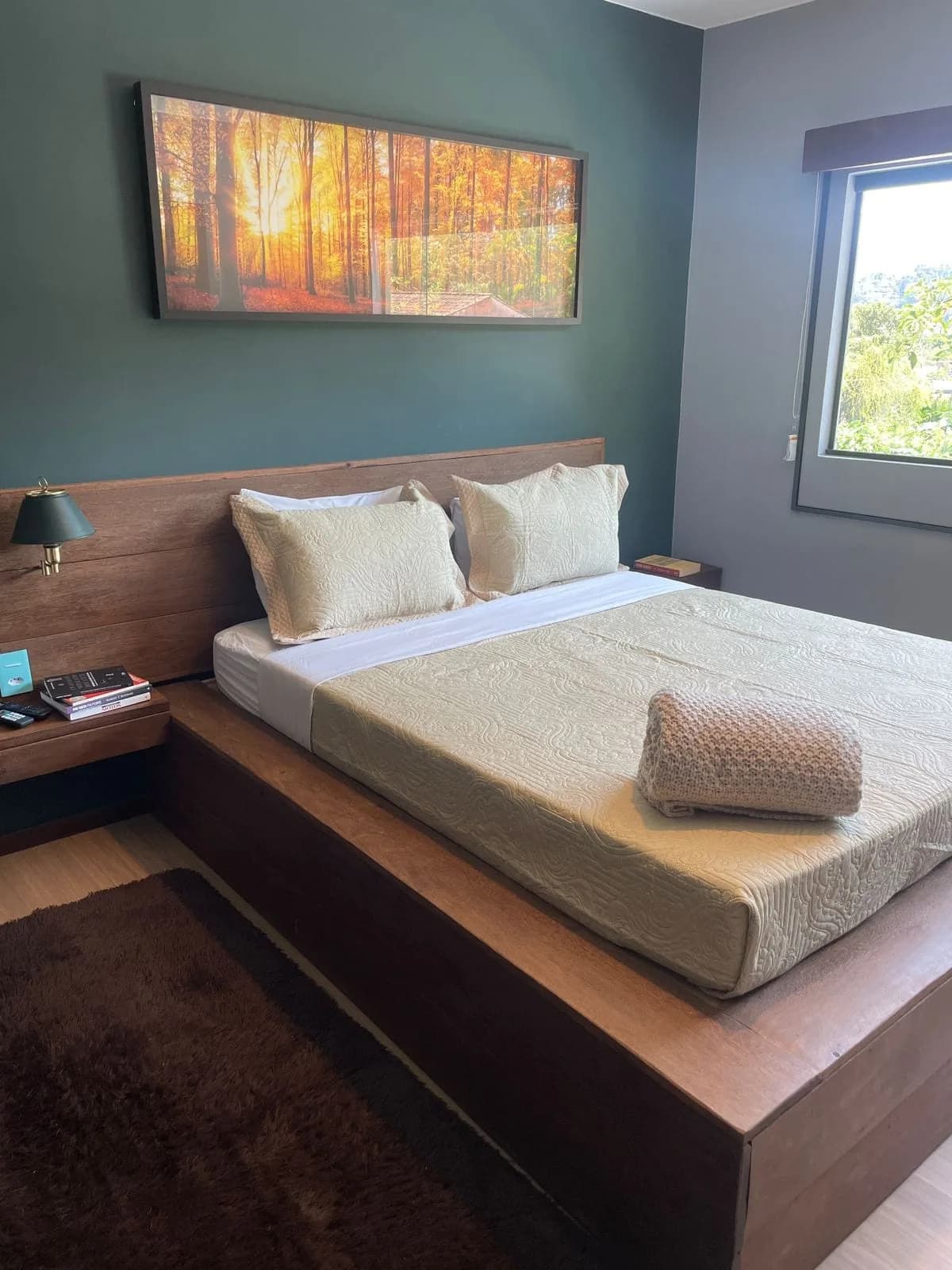 Loft Amazônia: Parede verde-musgo, quadro de floresta ao amanhecer e janela aberta para a mata.