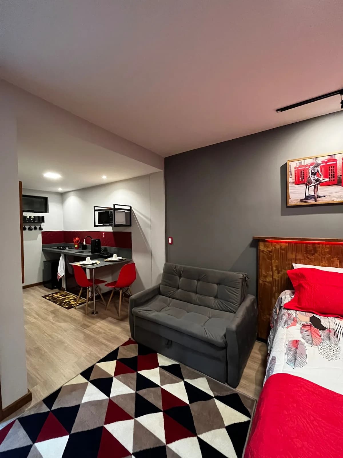 Loft Red Pepper: Cinza e vermelho, tapete geométrico e sofá de dois lugares de frente para a cama.